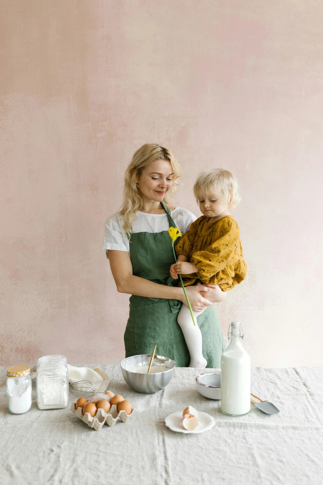 A mother holding her toddler at a kitchen table set with eggs and milk