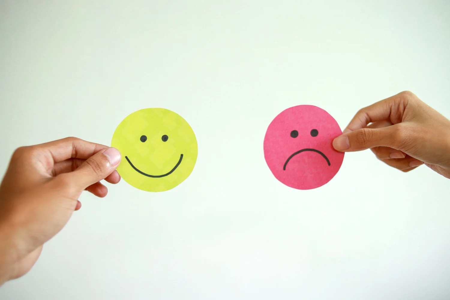 Two hands holding up a smiling face and a frowning face