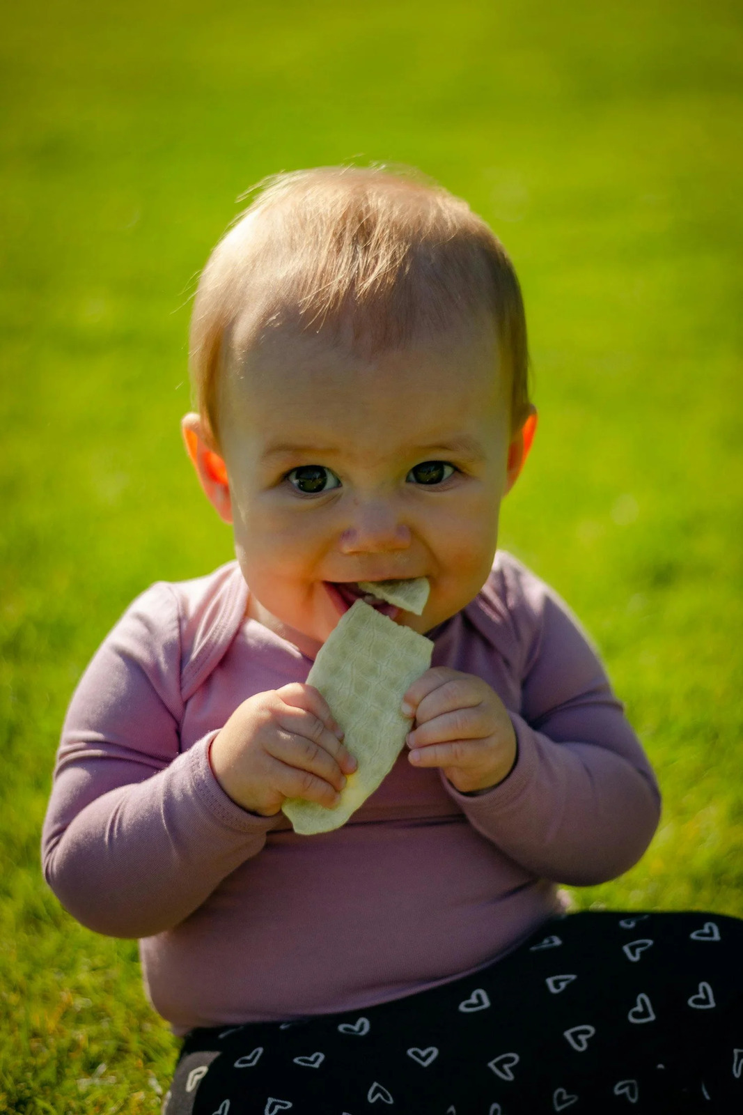 A baby chewing on a rice cake outdoors