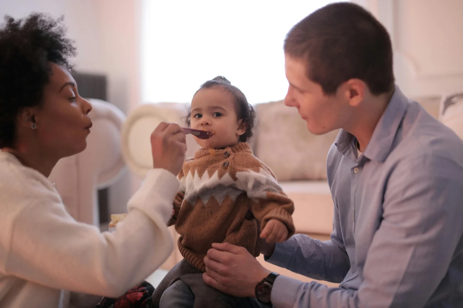 Two parents spoon-feeding their baby
