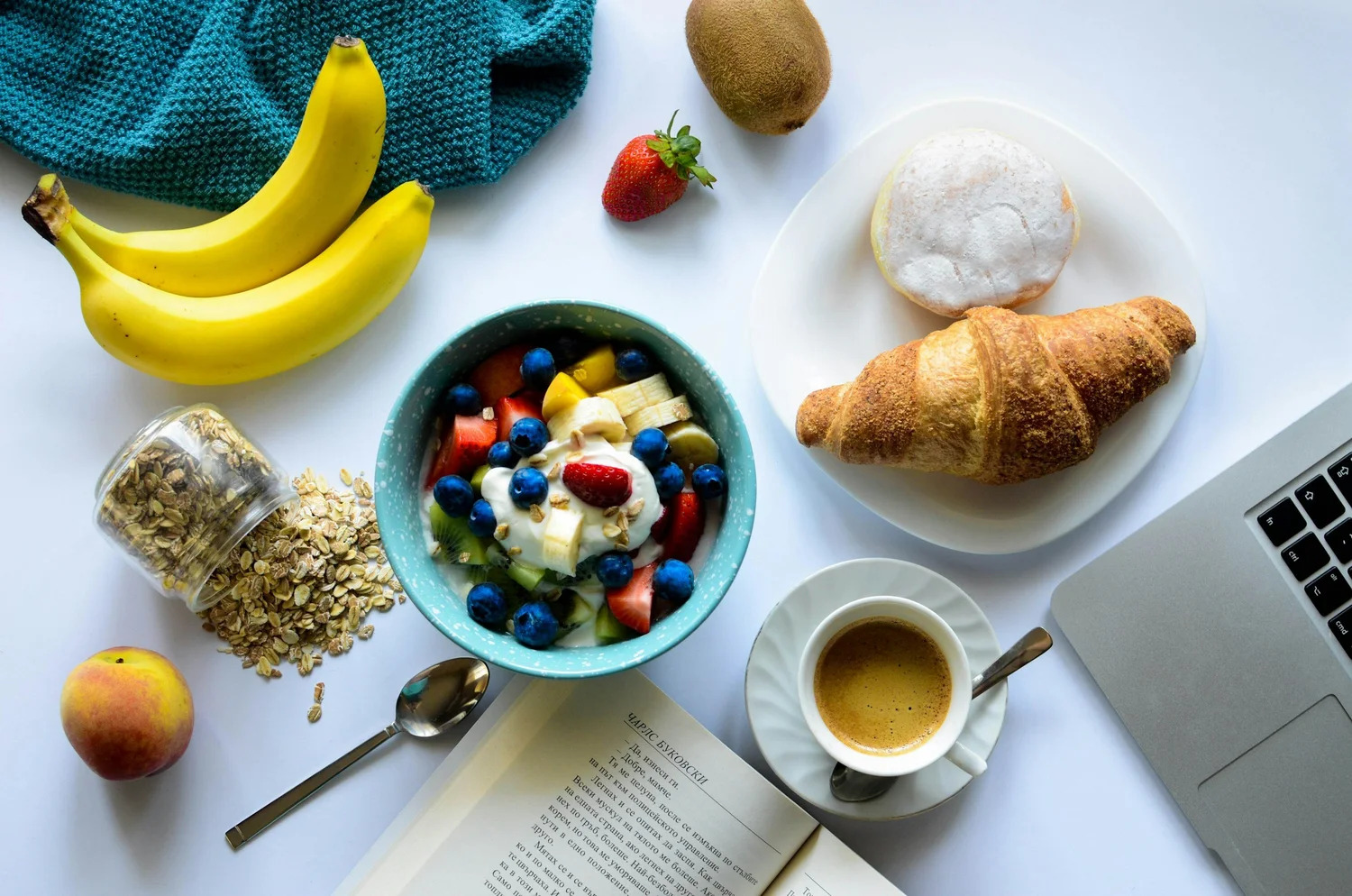 A breakfast spread of yogurt with fruit, oats, bananas, a croissant and coffee