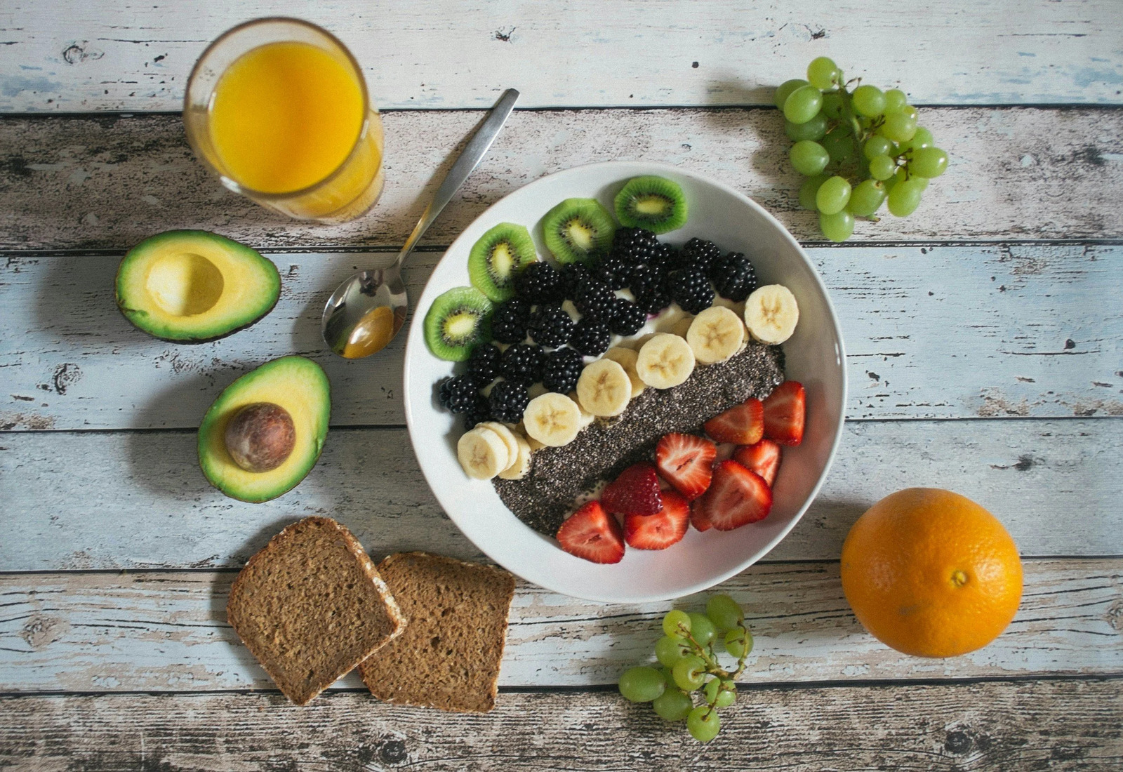 A breakfast bowl of fruit and chia beside avocado, toast and orange juice