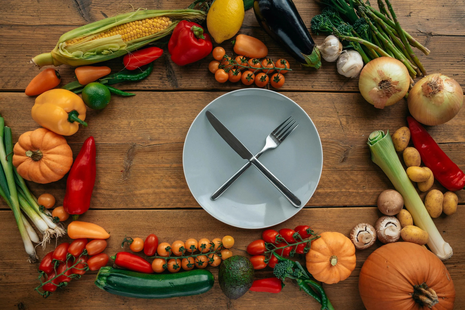 An empty plate with crossed cutlery ringed by fresh vegetables