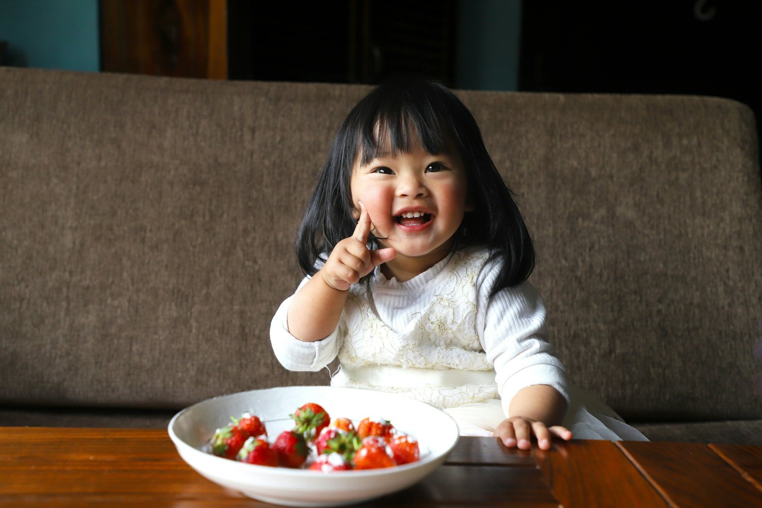 A smiling young girl at a table with a bowl of strawberries
