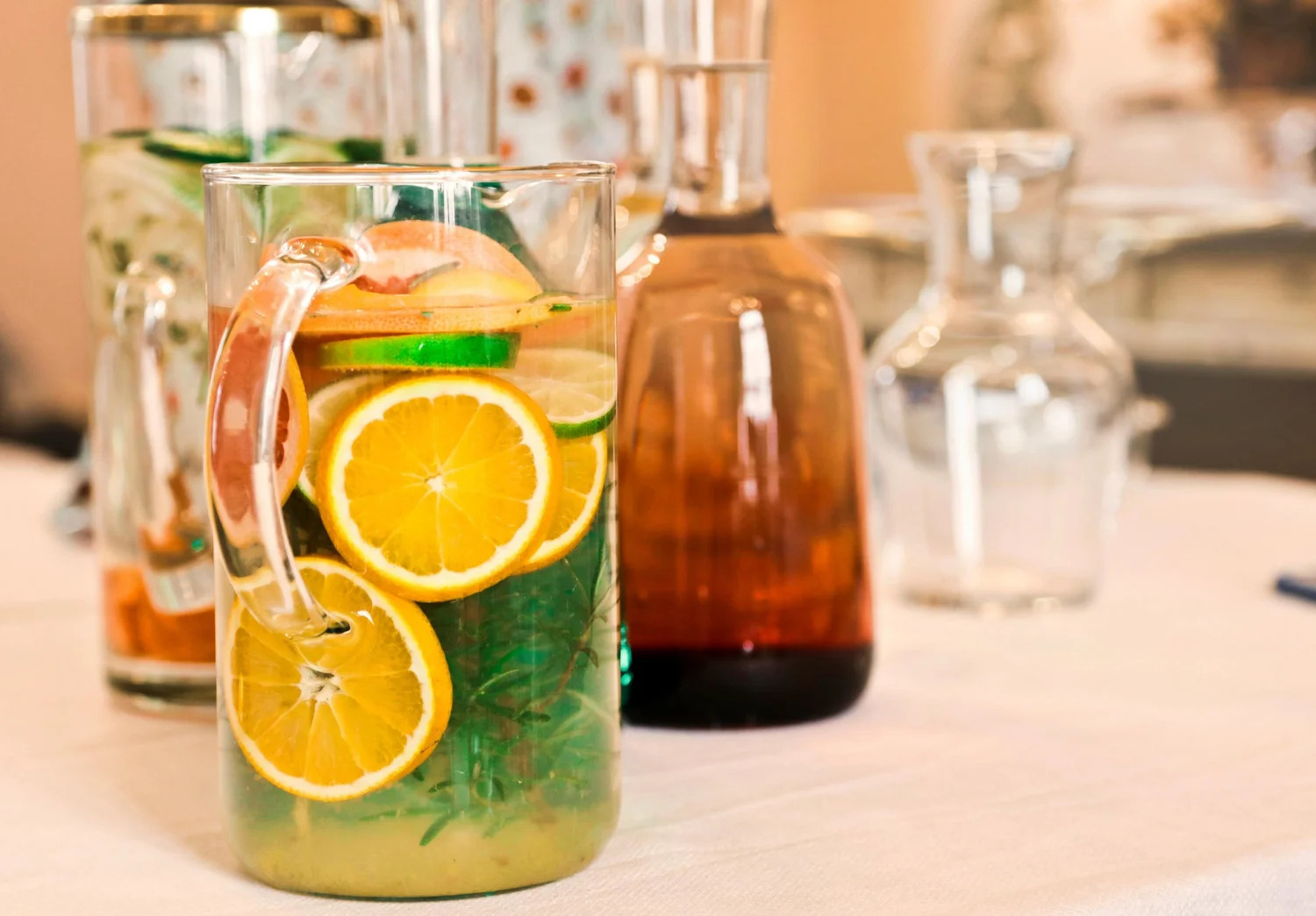 A pitcher of water with orange slices beside glass bottles