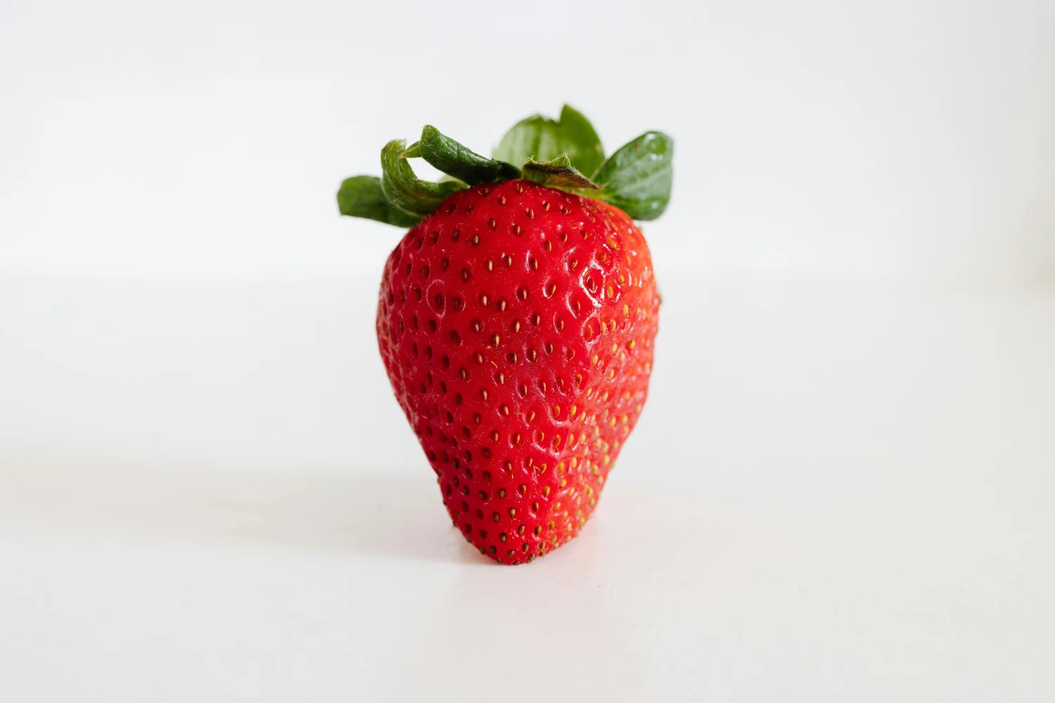 A single ripe strawberry on a white surface
