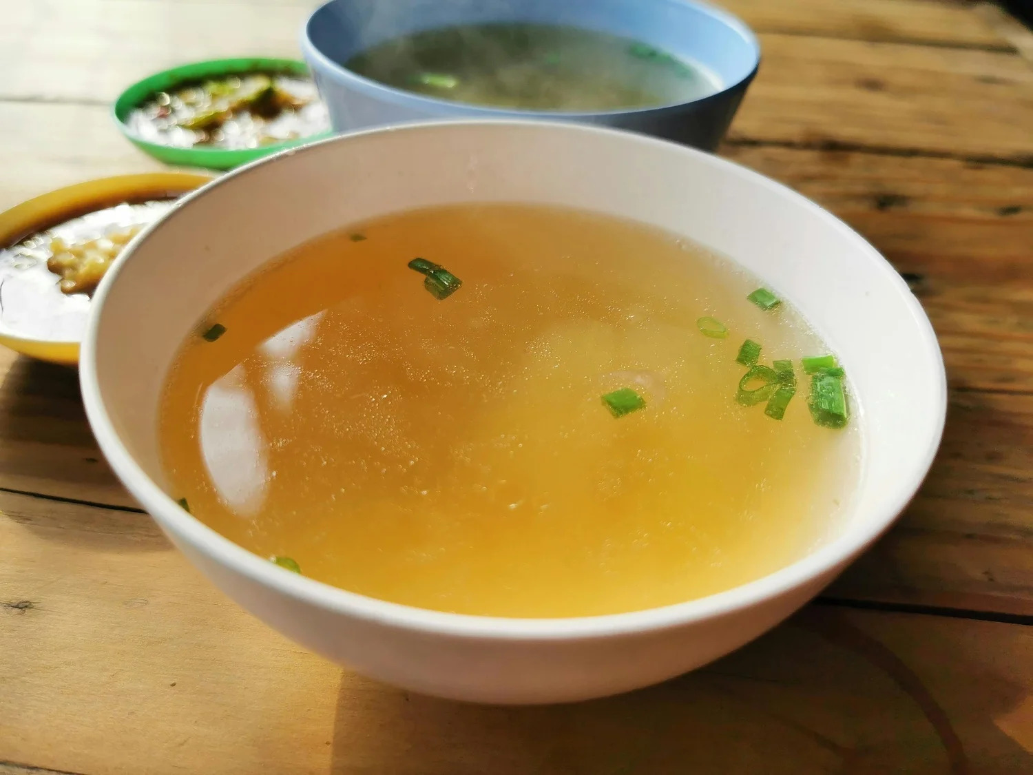 A bowl of clear broth on a wooden table