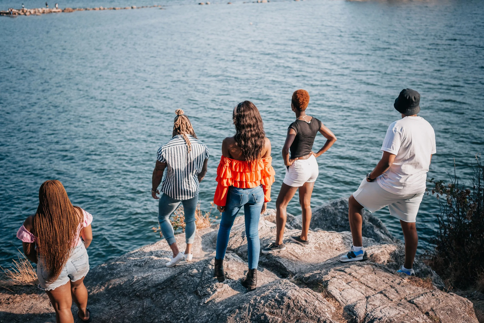 A group of teenagers standing together on rocks at the water's edge