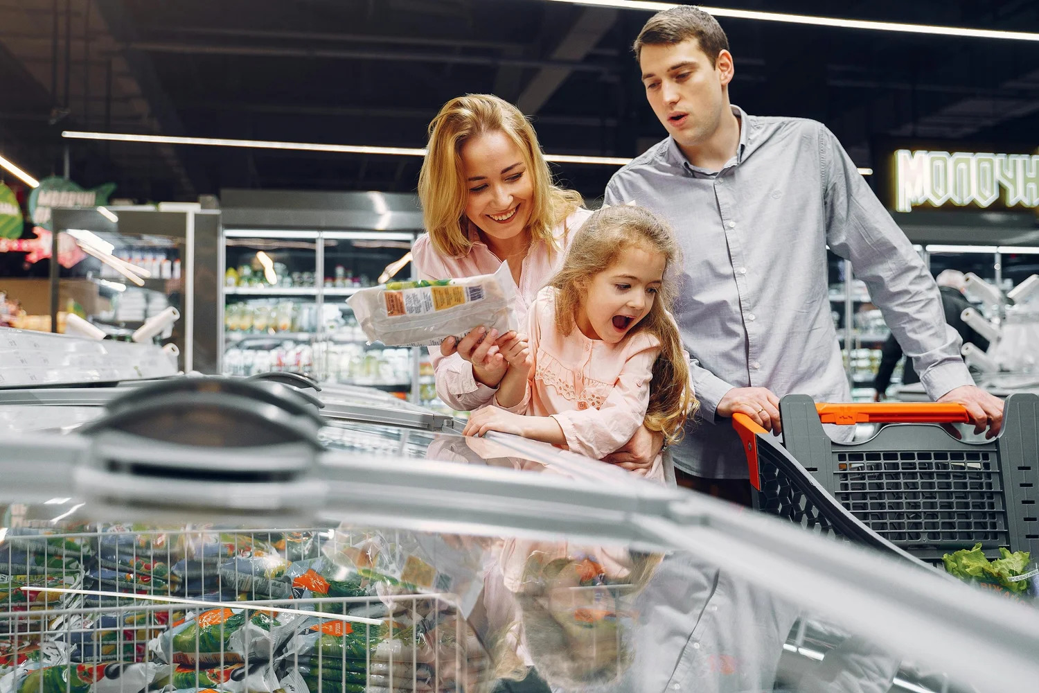Parents and a young girl shopping in a supermarket freezer aisle