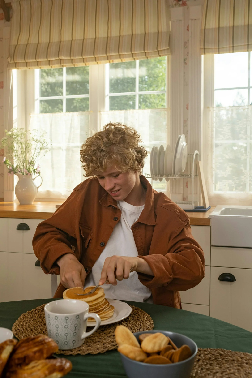 A teenager eating a stack of pancakes at the kitchen table