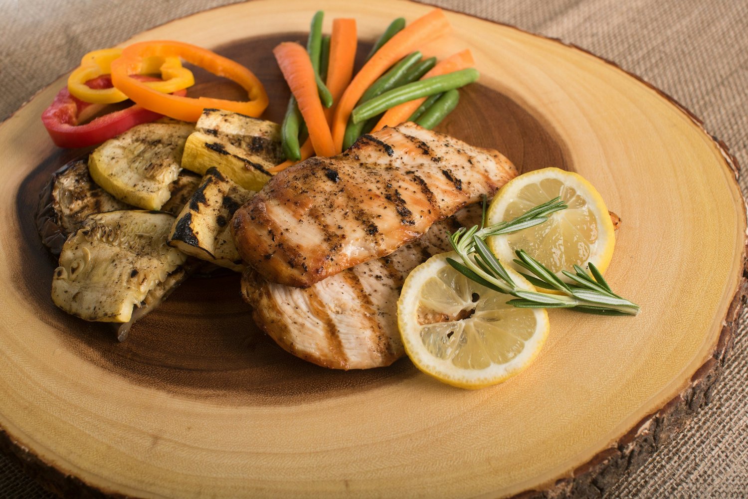 Grilled chicken with grilled squash, carrots, green beans and lemon on a wooden board