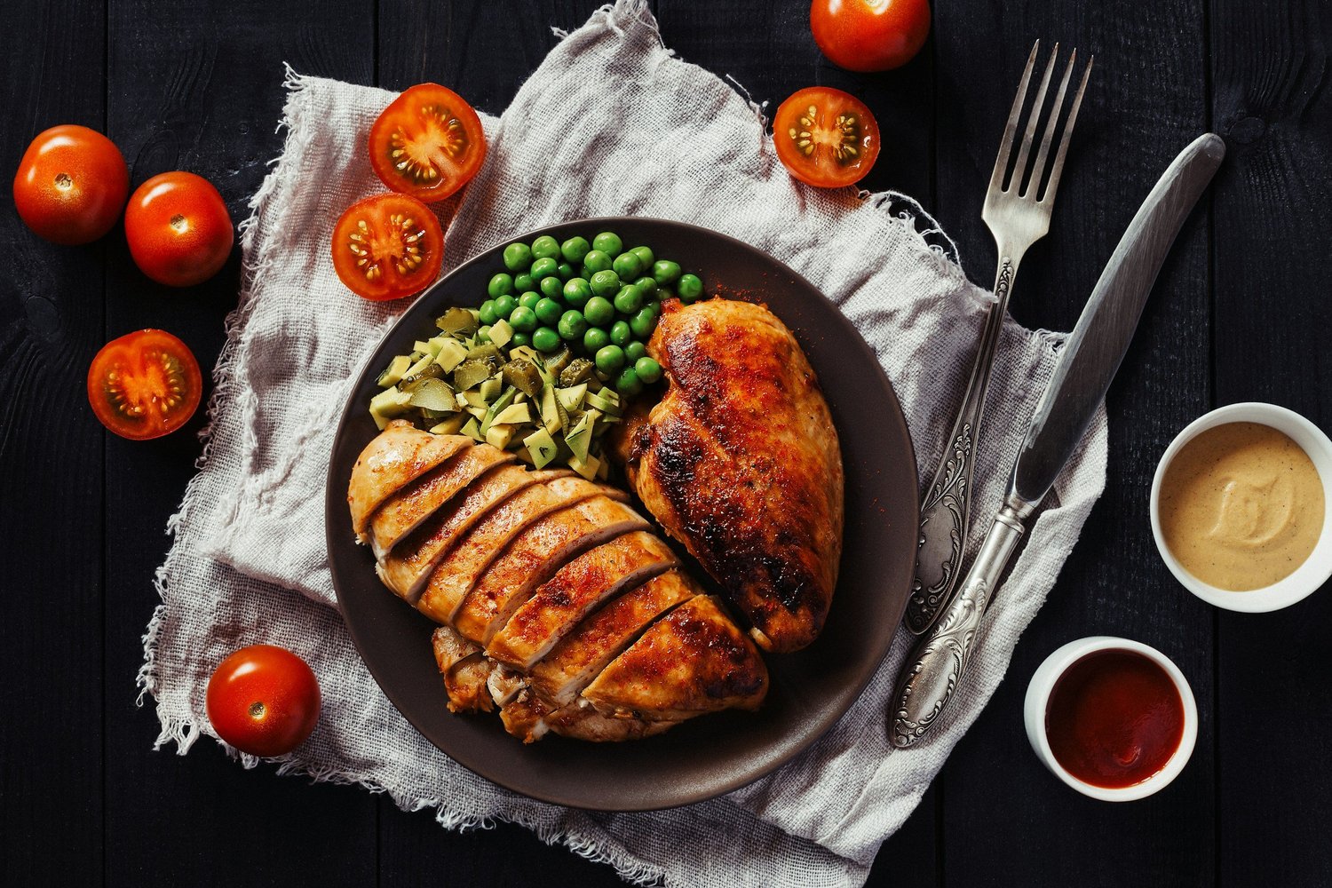 Sliced roasted chicken breast with peas and diced avocado on a dark plate