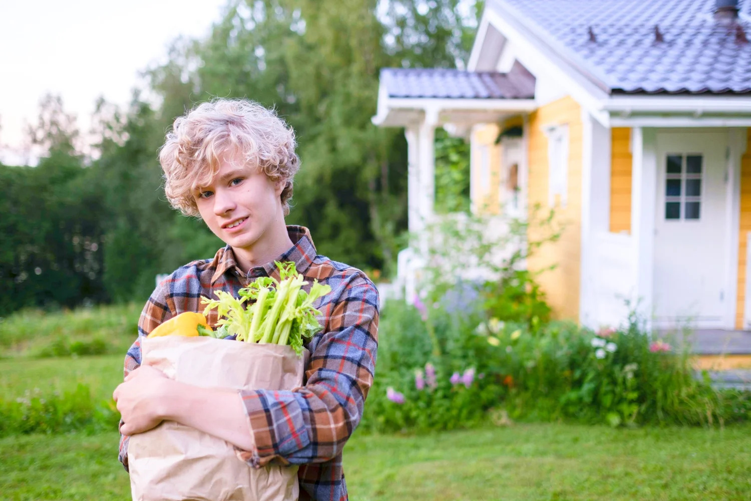 A teenager carrying a paper bag of groceries outside a house