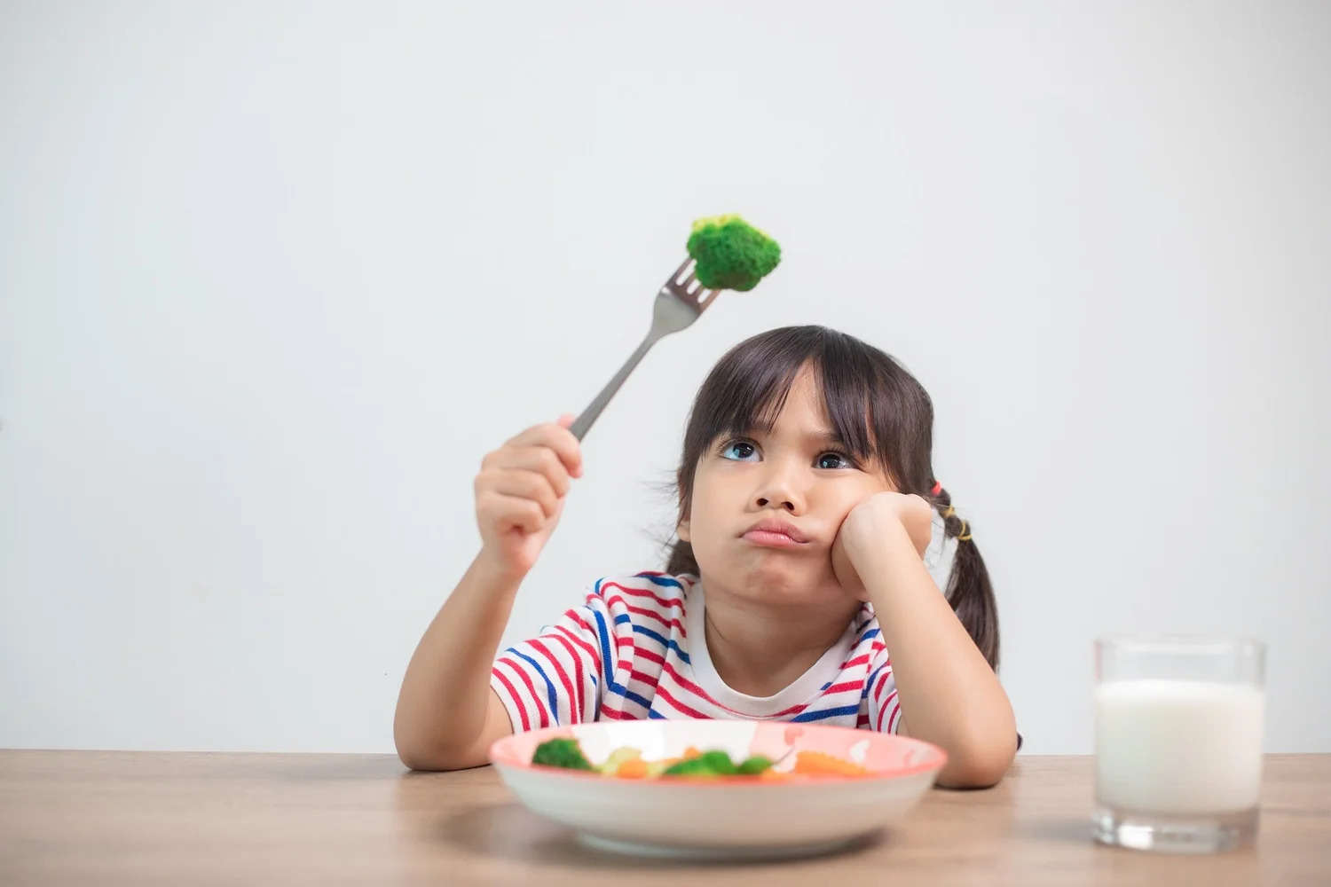 A young girl frowning at a piece of broccoli on her fork