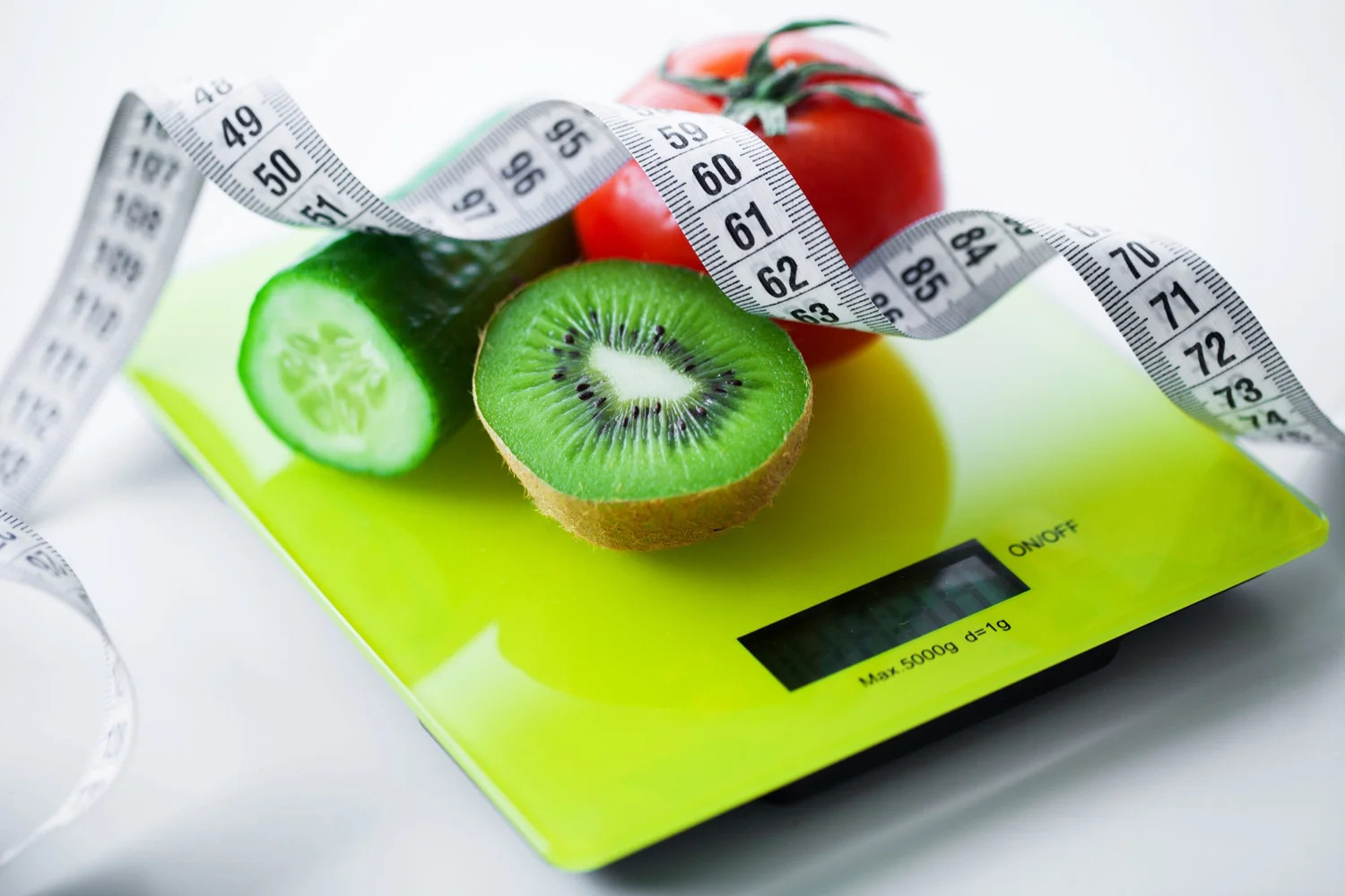 Kiwi, tomato and cucumber on a kitchen scale wrapped in measuring tape