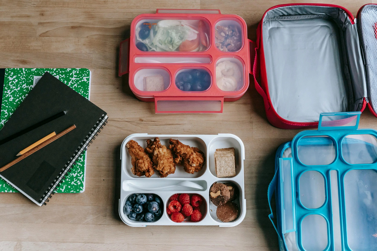 Packed bento-style lunchboxes with snacks and fruit beside a notebook
