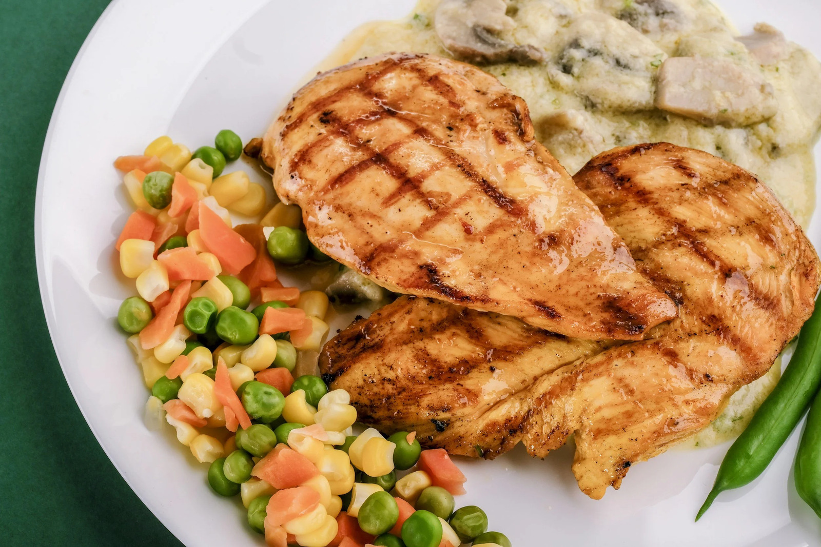 Grilled chicken breasts with peas, carrots and corn on a plate