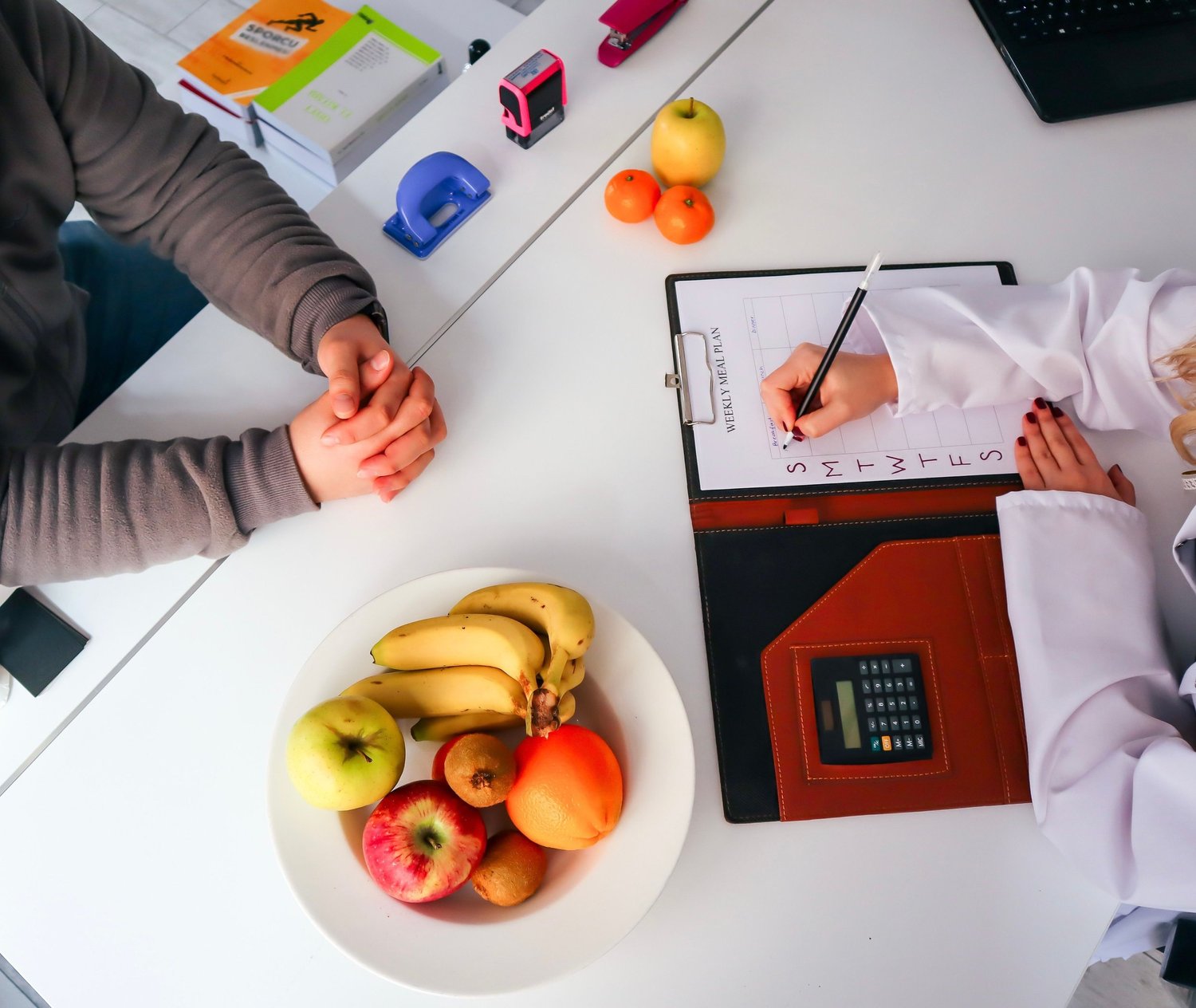 Overhead view of a dietitian filling in a weekly meal plan across a desk from a client