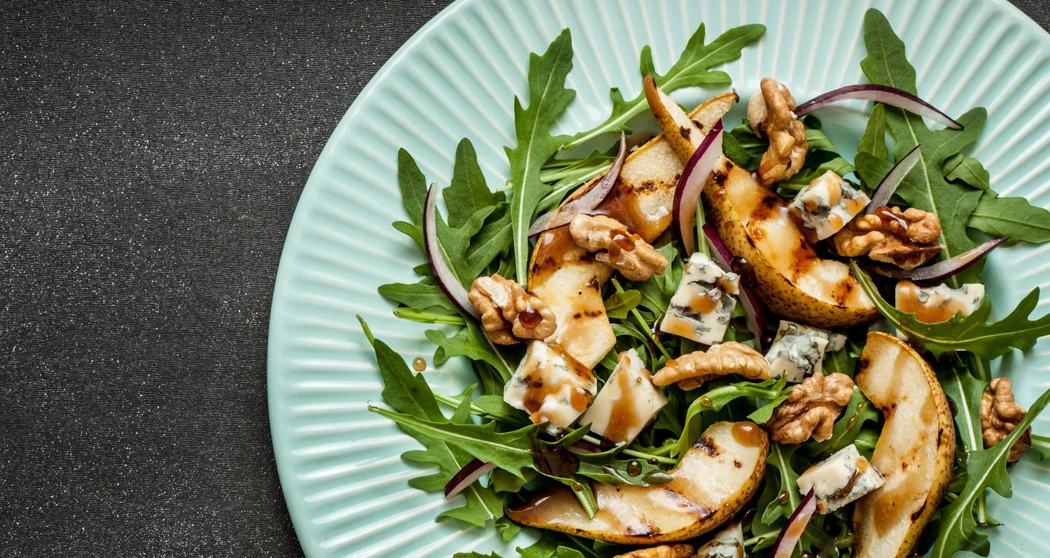 An overhead view of an arugula salad with grilled pear, walnuts and blue cheese