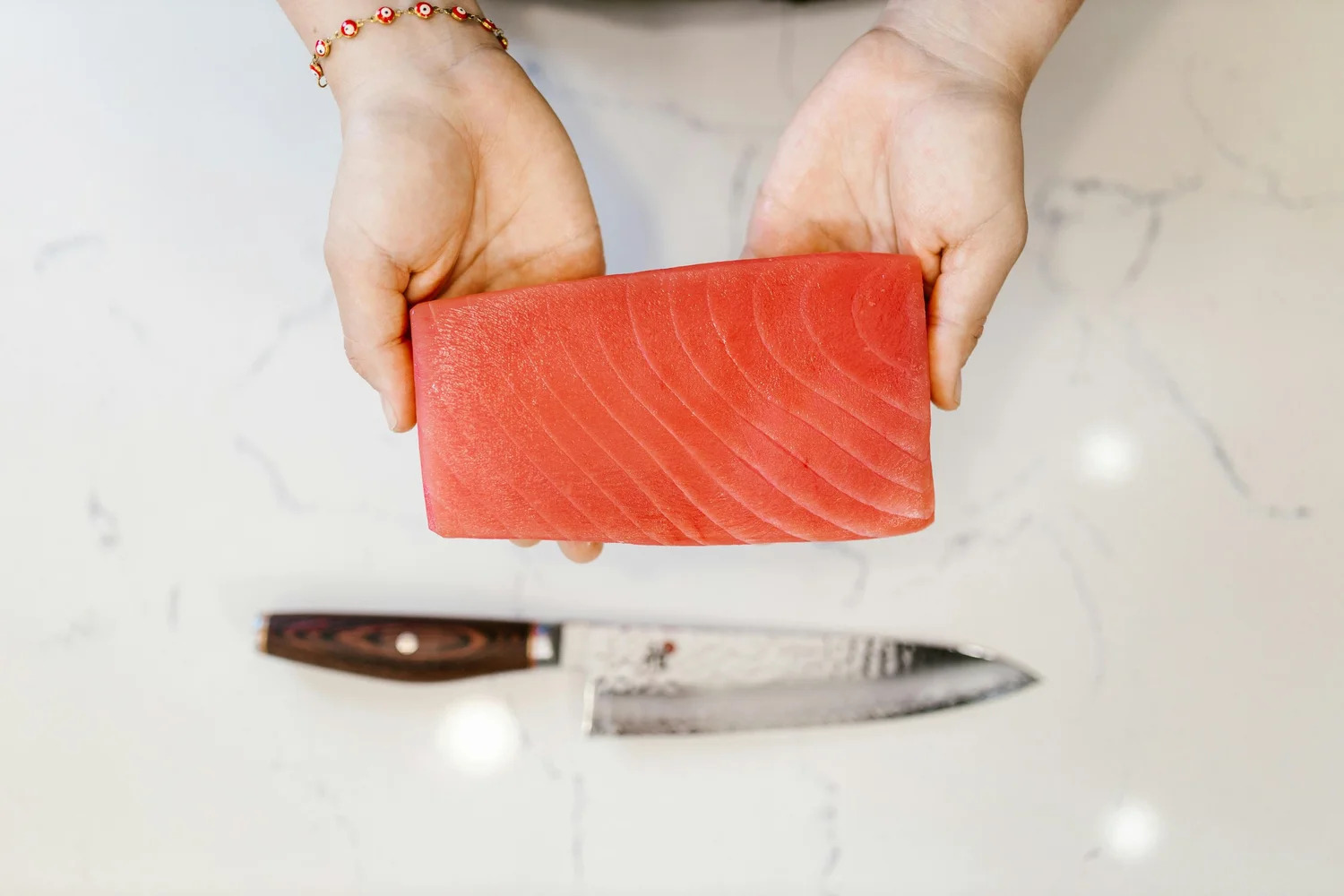 Hands holding a raw salmon fillet above a kitchen knife