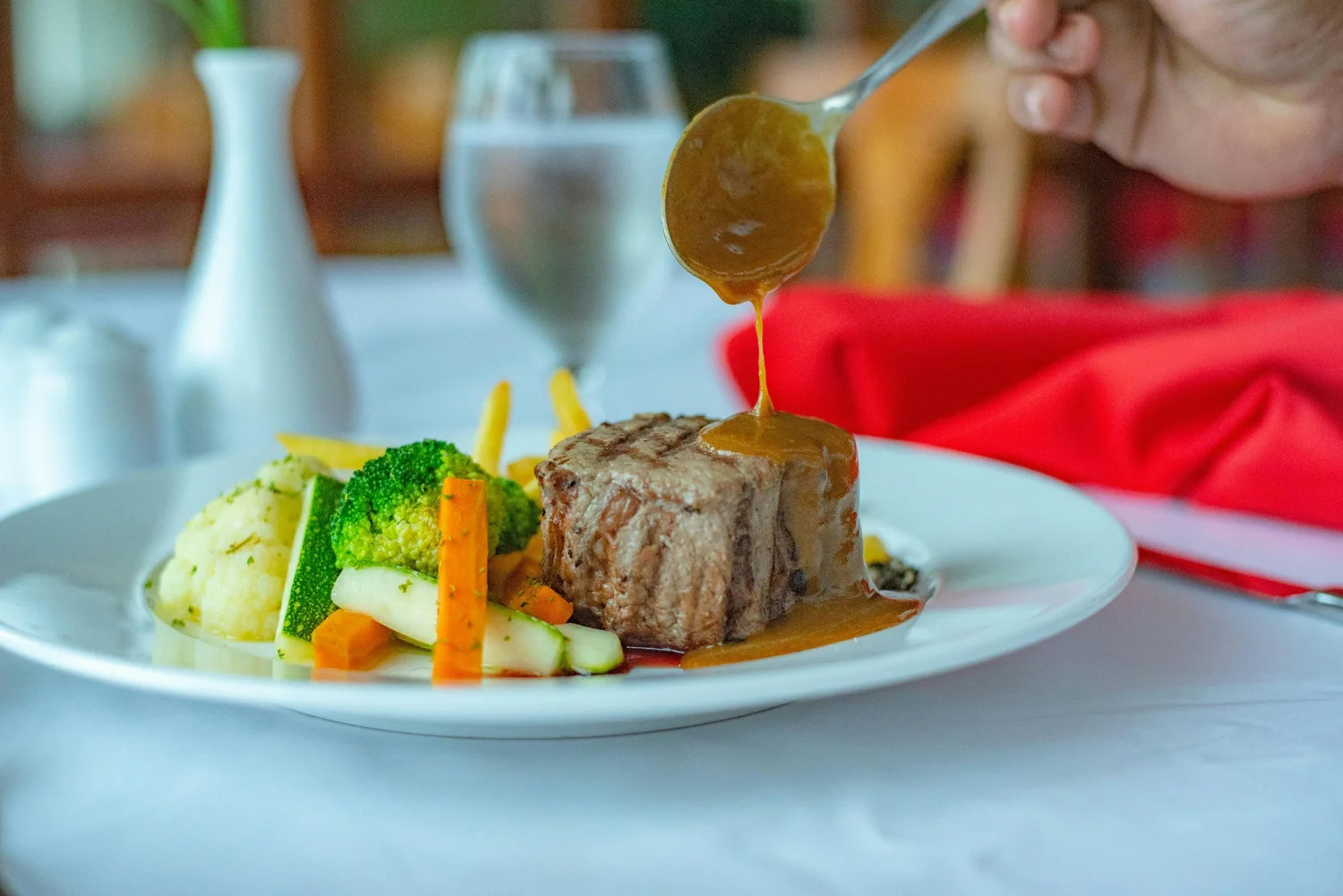 Sauce being poured over a plated steak with vegetables