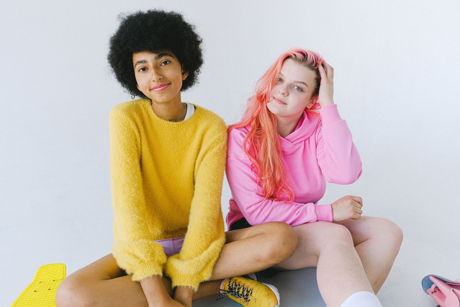Two teenage girls sitting together on the floor against a white wall