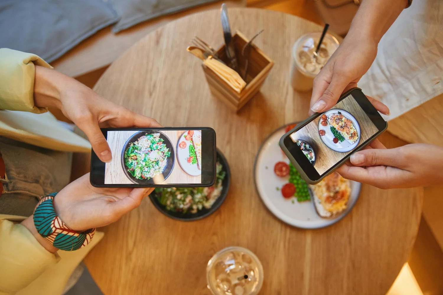 Two people taking phone photos of their meals at a cafe table