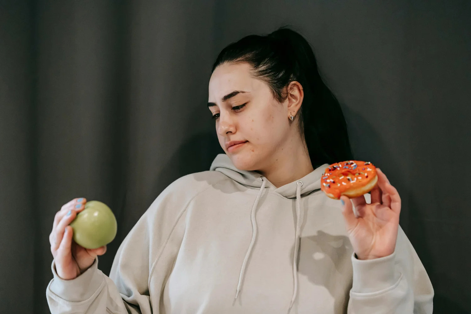 A woman weighing up an apple in one hand and a doughnut in the other