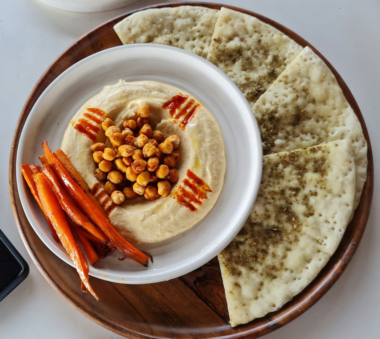 Hummus topped with roasted chickpeas beside carrots and pita wedges