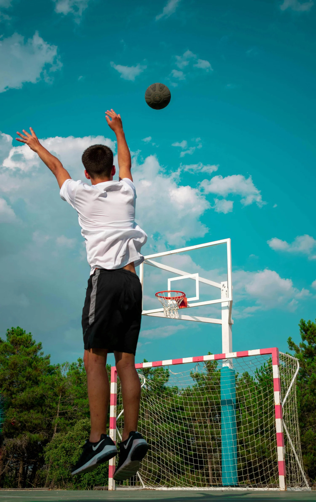 A teenager leaping to shoot a basketball on an outdoor court