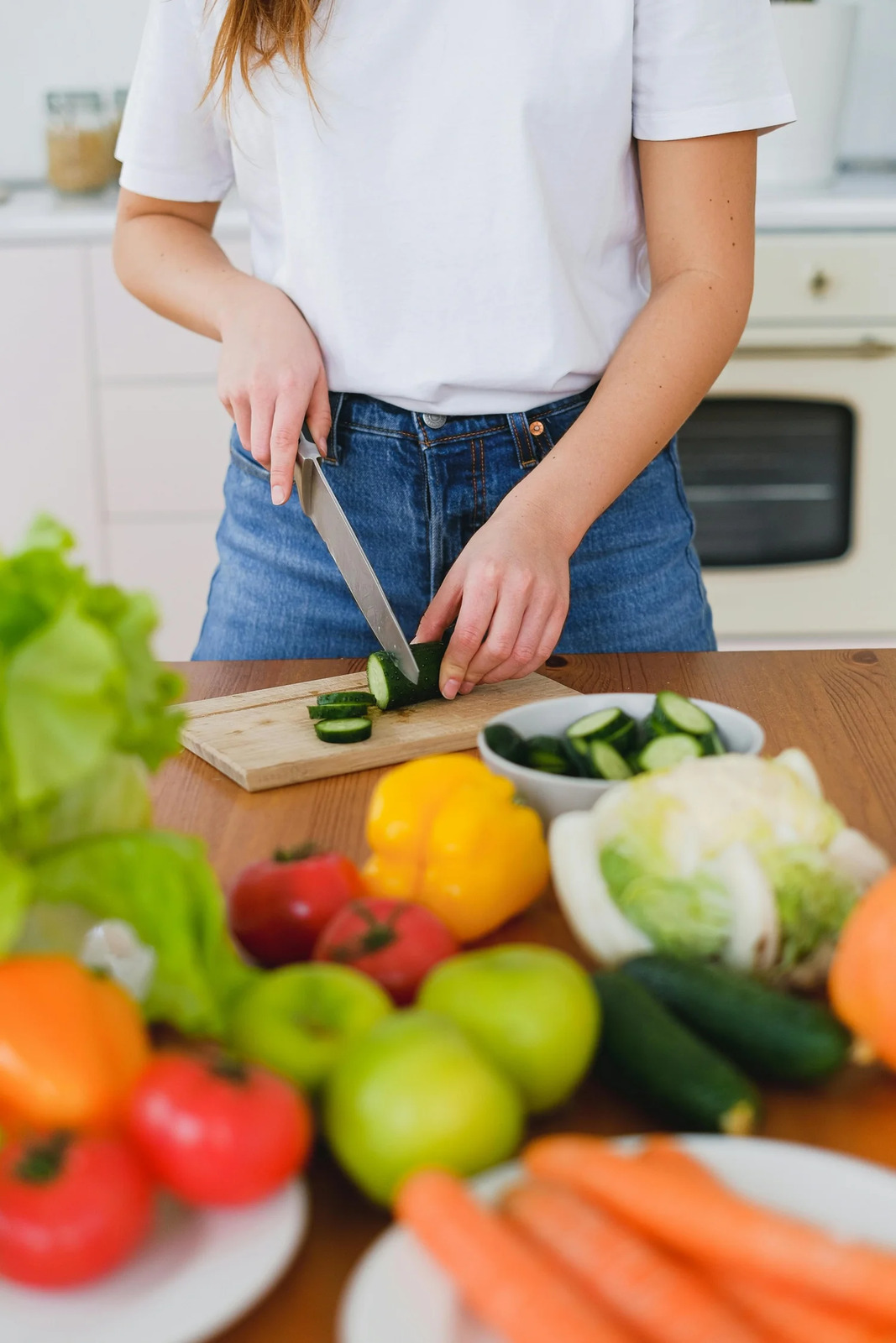 A person slicing cucumber beside a board of fresh vegetables
