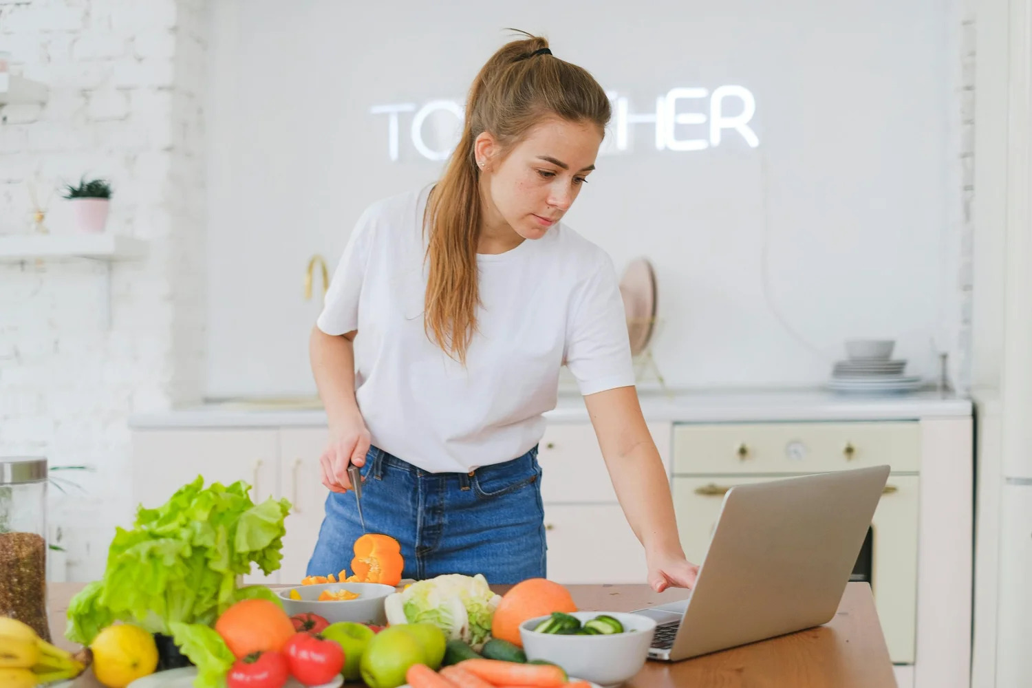 A woman preparing vegetables at her kitchen counter beside a laptop