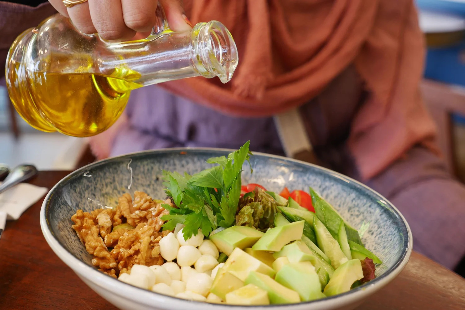 Olive oil being poured over a grain bowl with avocado and greens