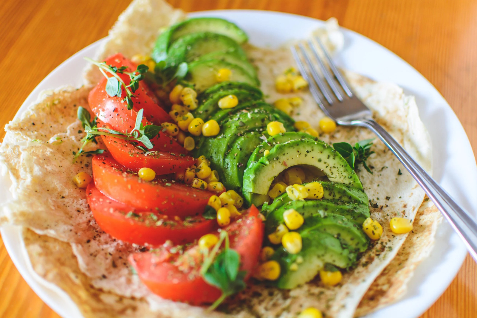 A plate of sliced tomatoes, avocado and corn