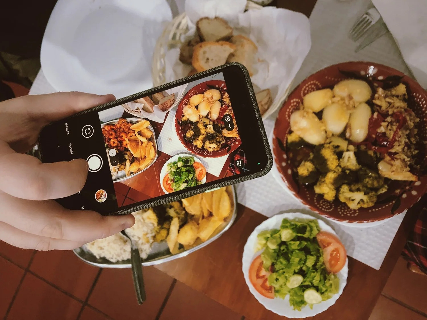 A smartphone photographing a table of shared dishes from above