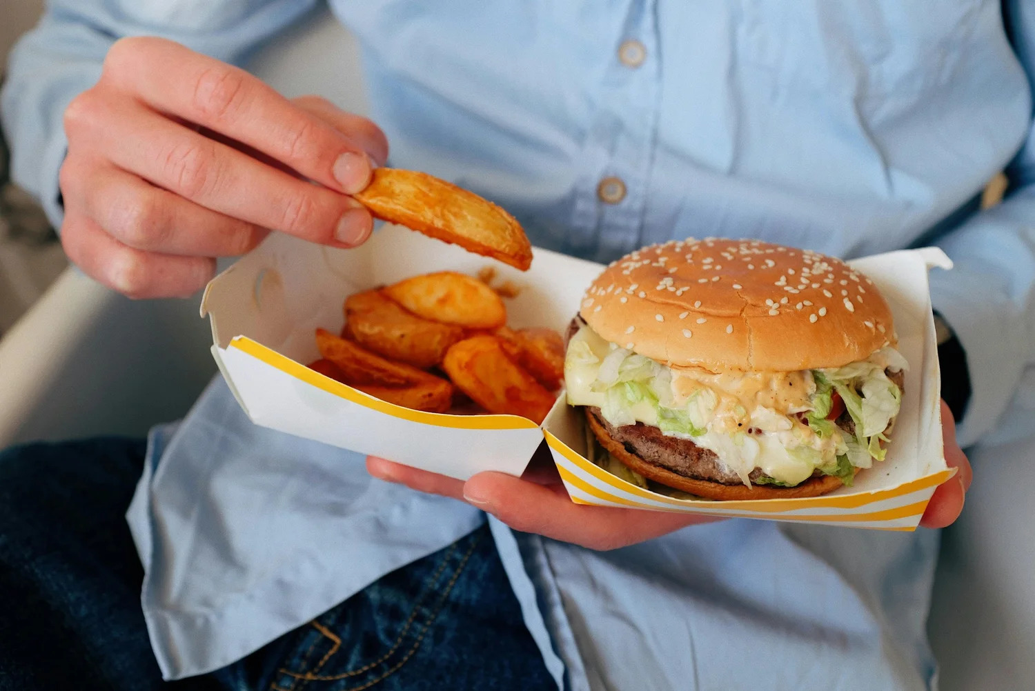 A person holding a burger and fries in a takeout box