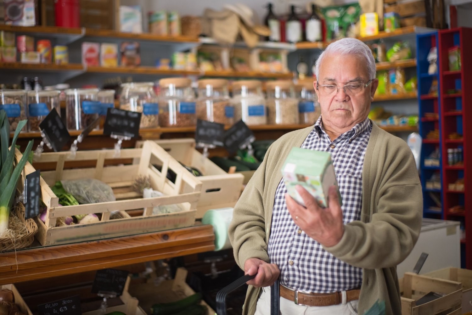 An older man reading the label on a box in a grocery store