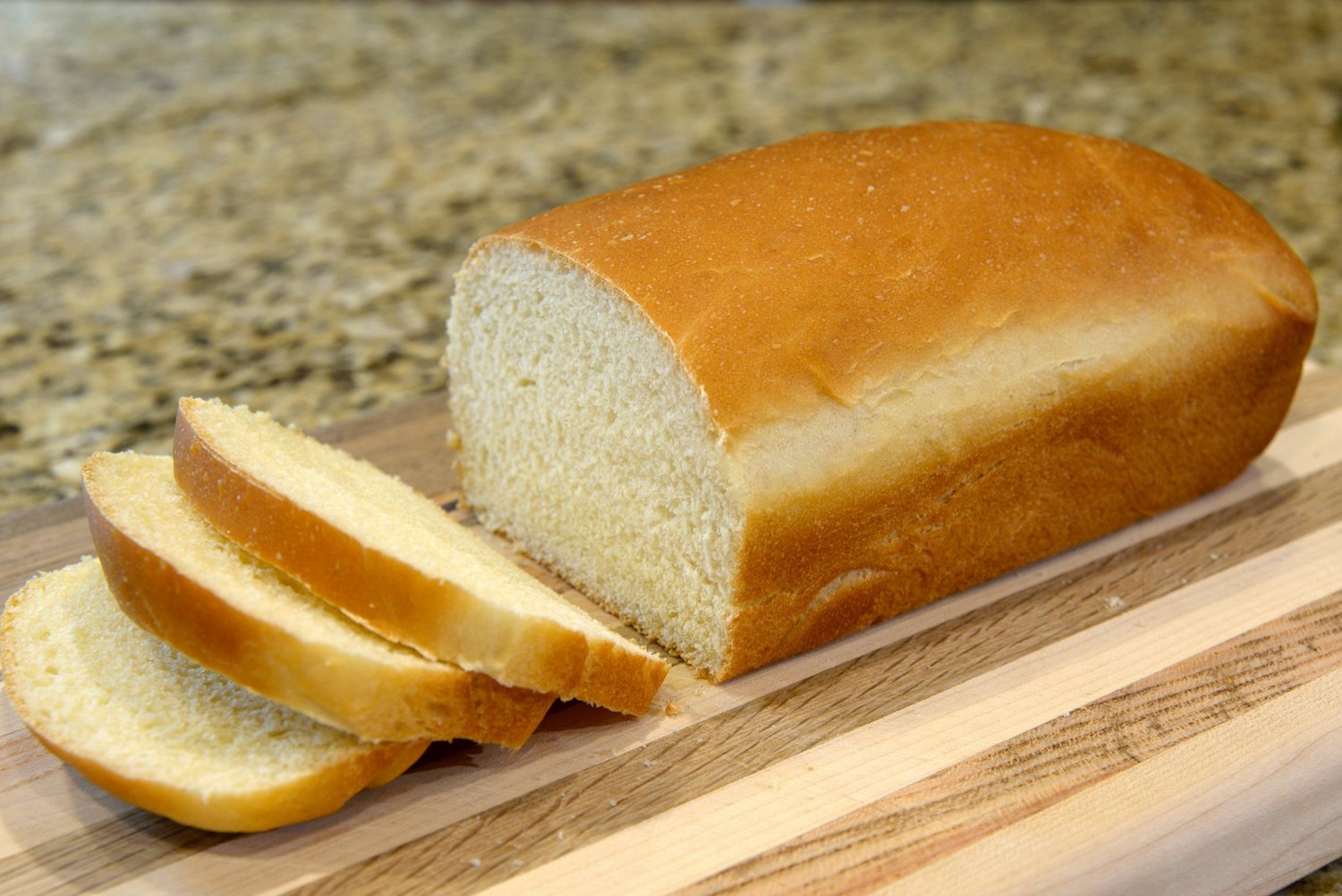 A sliced loaf of white bread on a wooden cutting board
