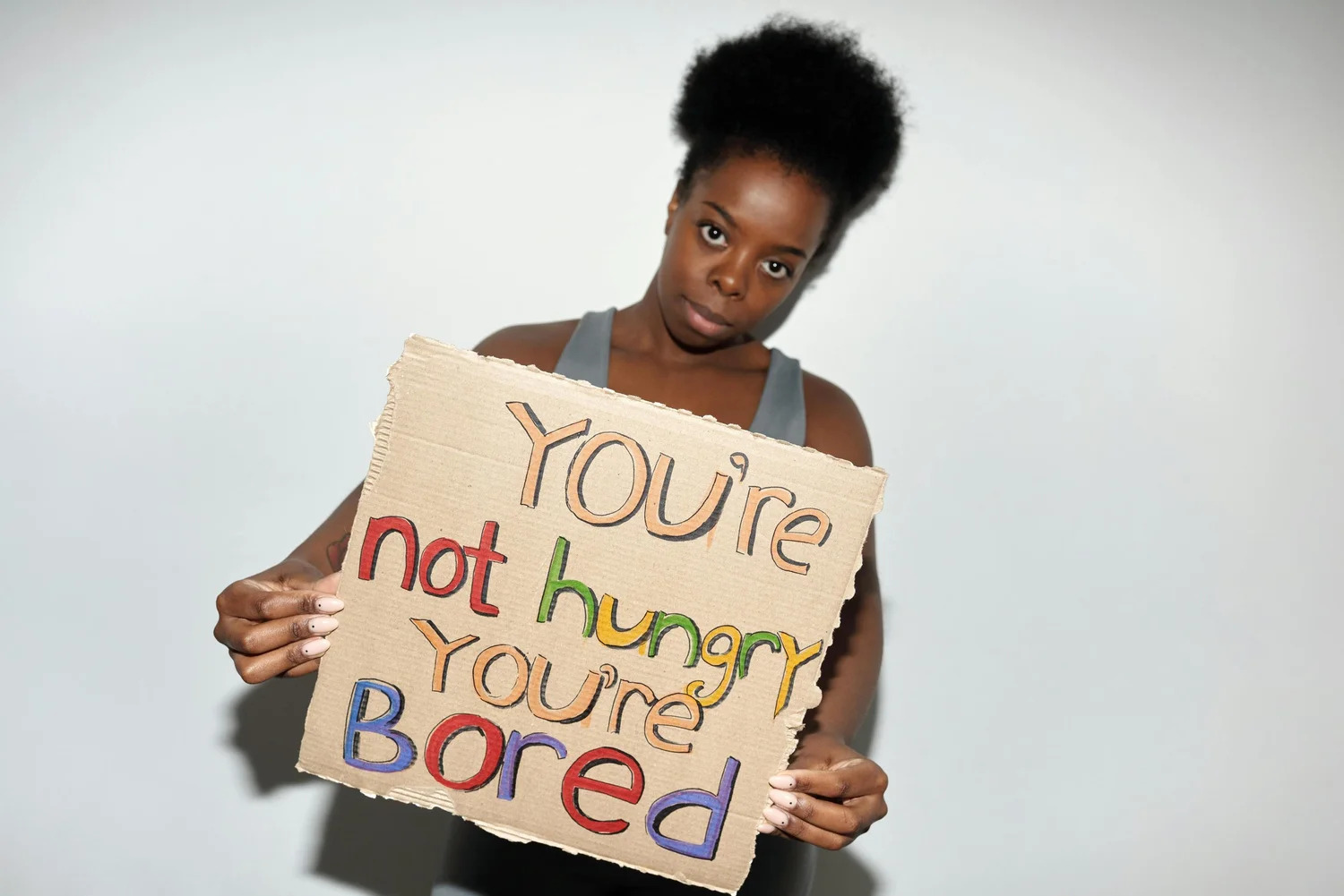 A woman holding a handwritten sign that reads You're not hungry, you're bored