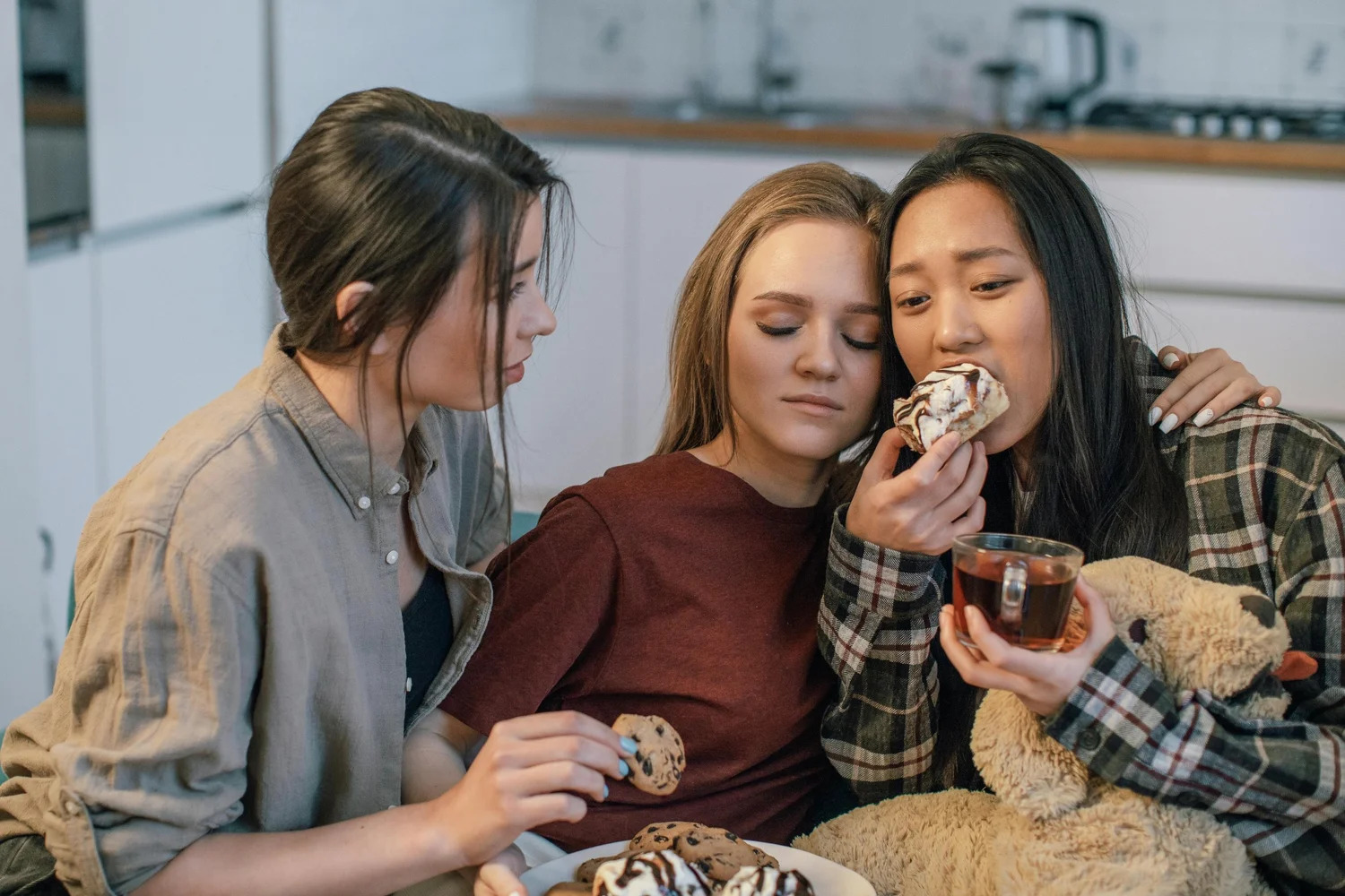 Three friends sitting close together sharing snacks