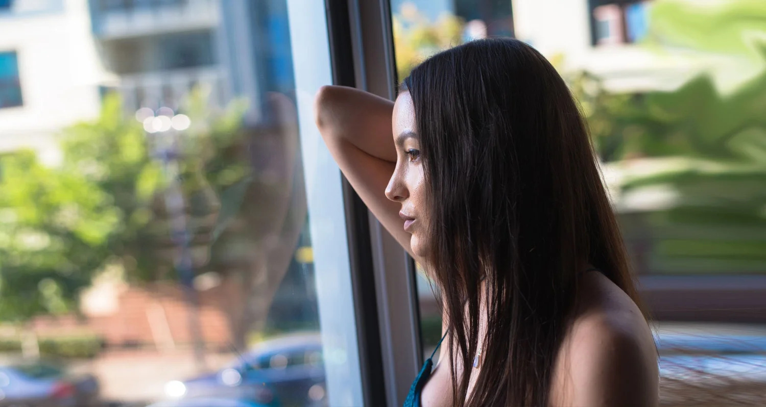 A woman gazing out a window, resting her head on her hand