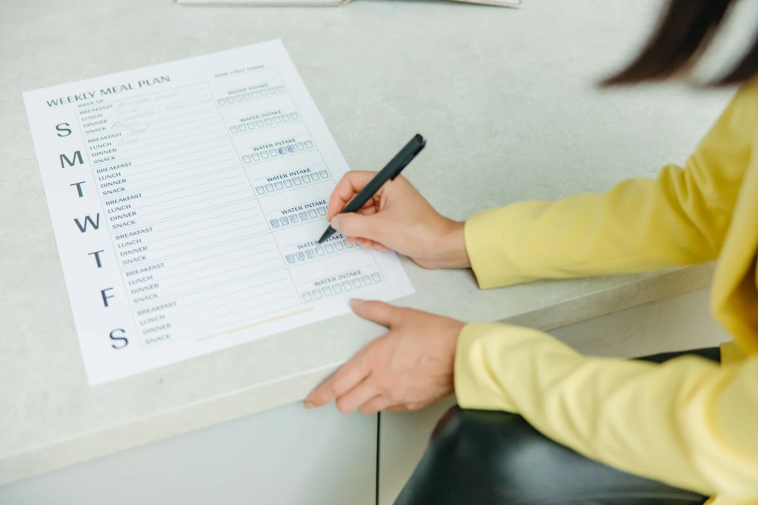 A person filling in a written weekly checklist at a table