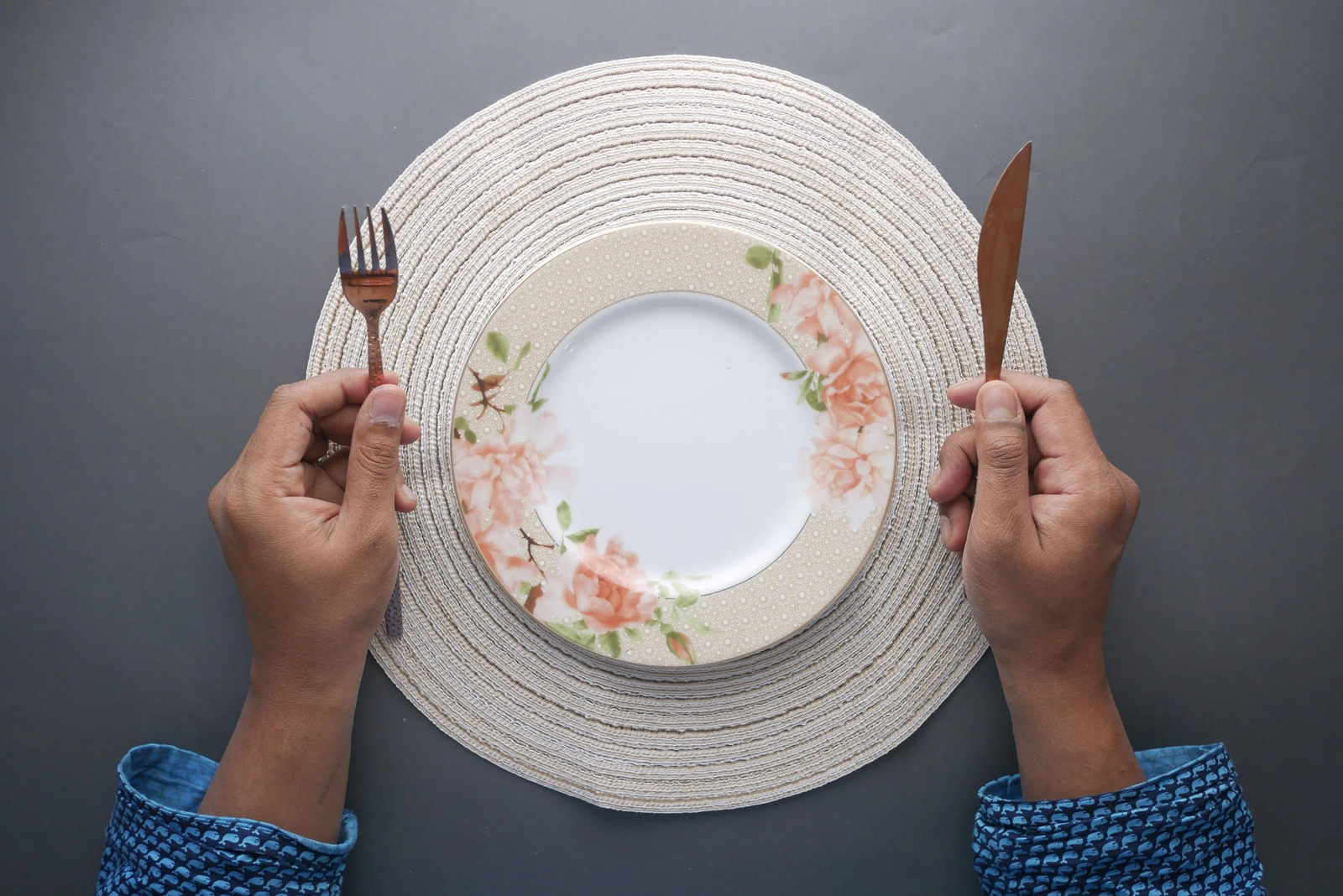 Hands holding a fork and knife on either side of an empty plate