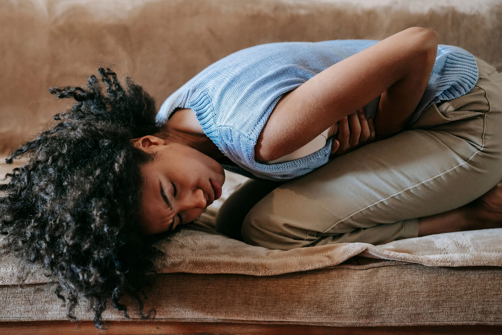 A woman curled up on a sofa, holding her stomach