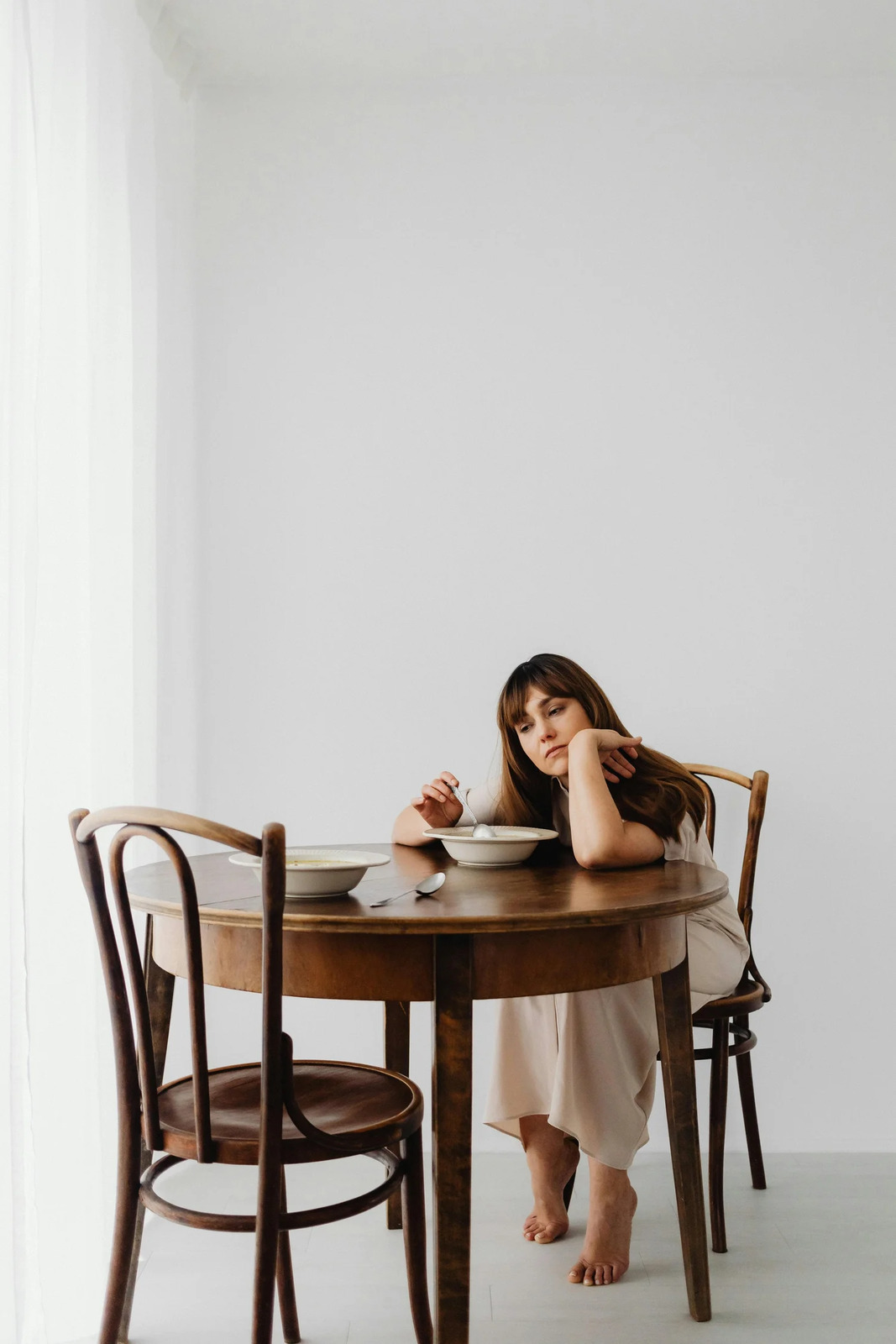 A woman sitting alone at a small dining table, looking pensive