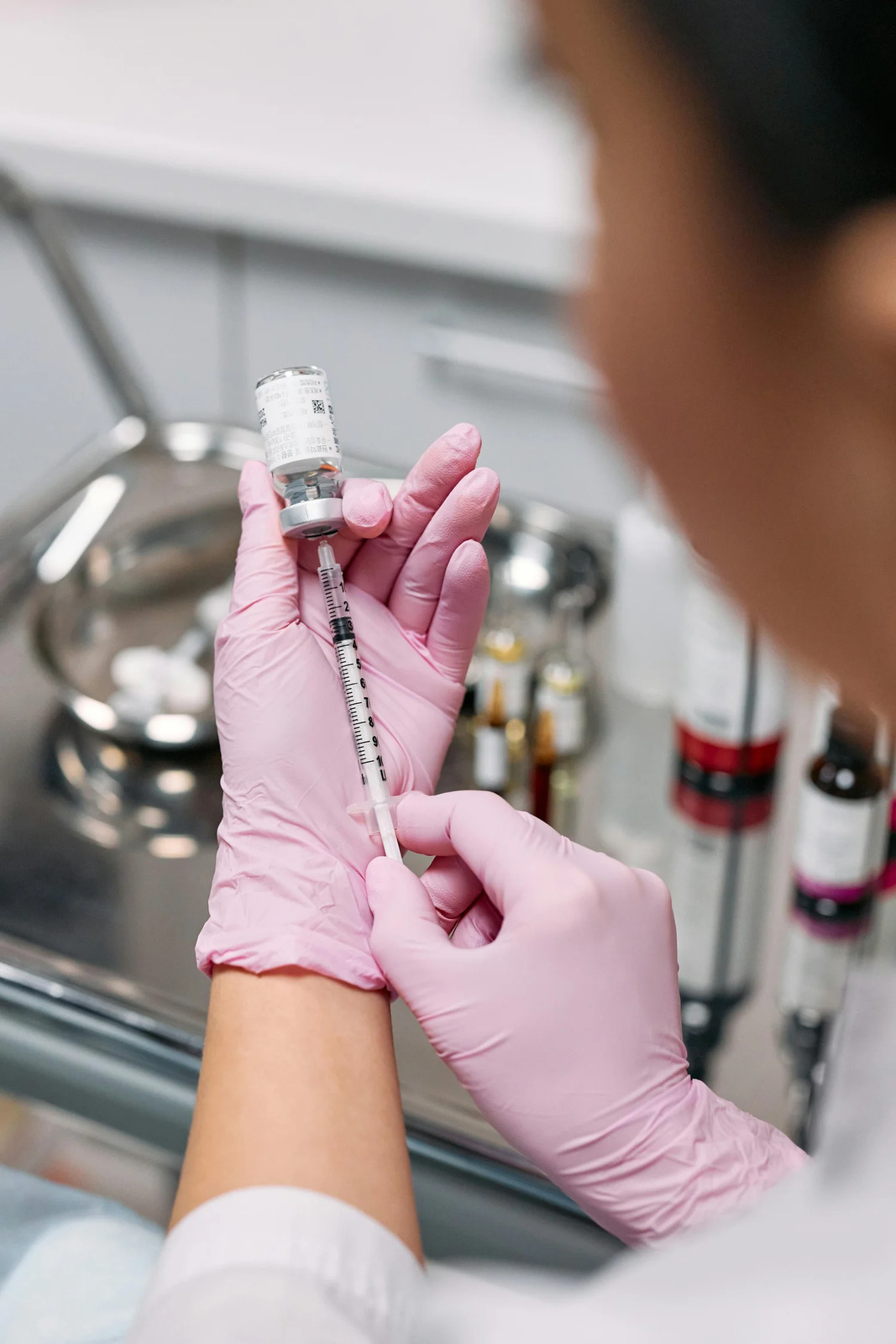 Gloved hands filling a syringe from a small glass ampoule
