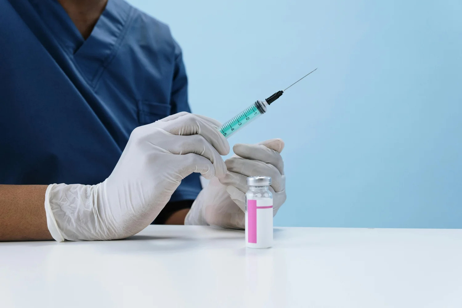 Gloved hands drawing medication from a vial into a syringe
