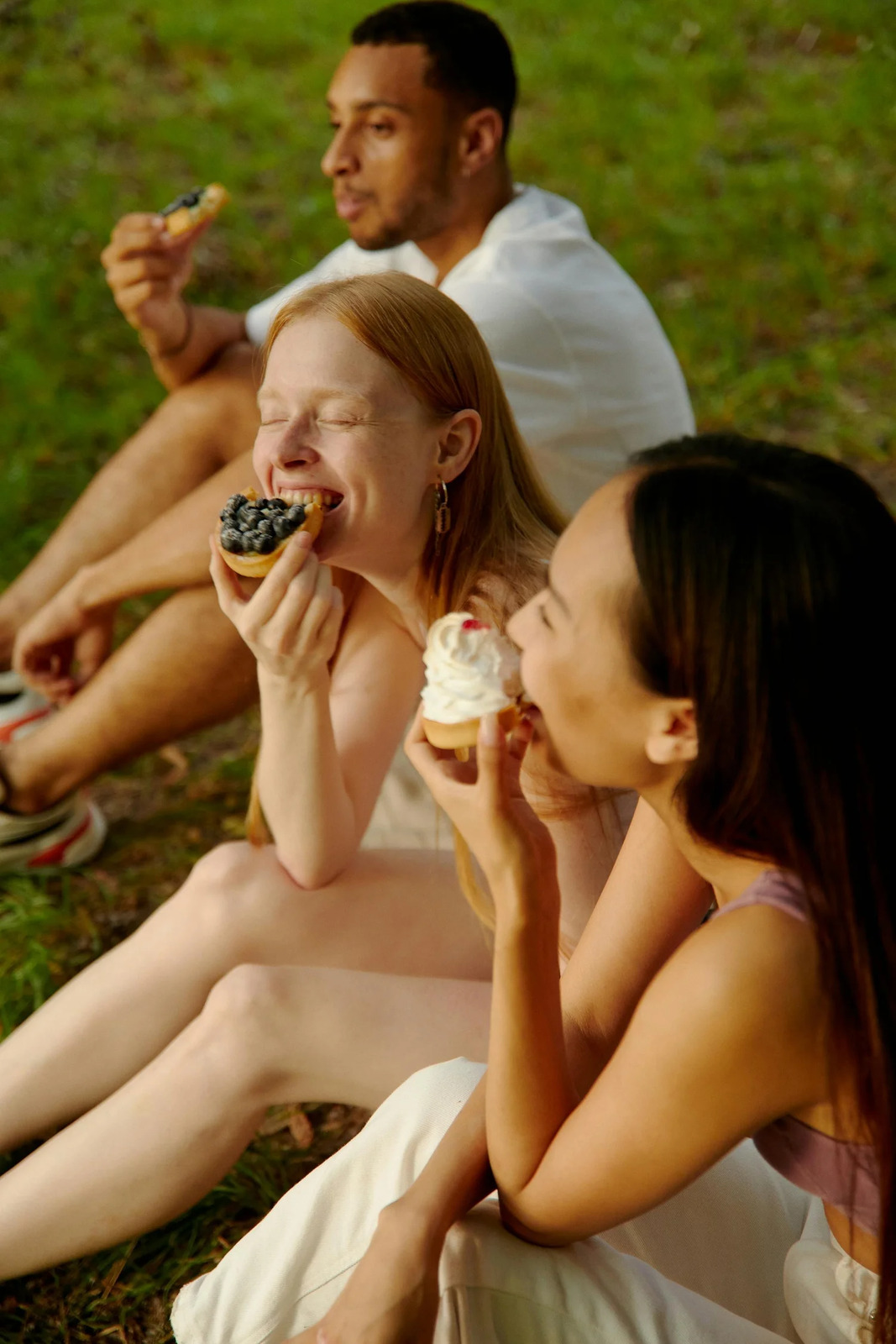 Friends laughing and eating cupcakes together outdoors