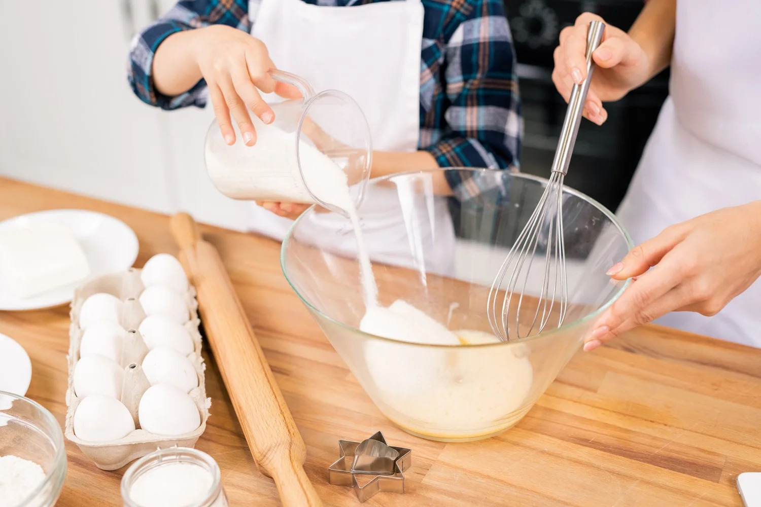 A child pouring sugar into a mixing bowl while baking