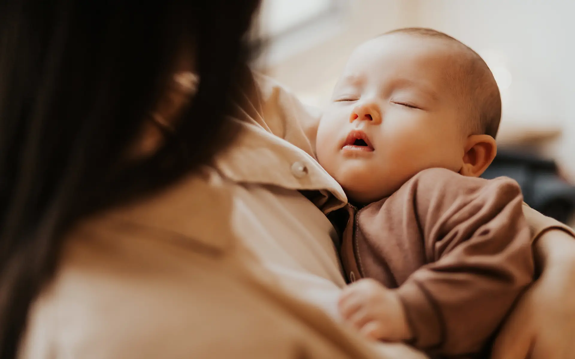 A parent holding a sleeping baby against their shoulder in soft natural light